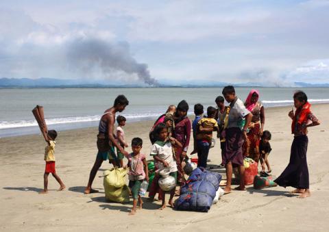 Smoke is seen on Myanmar's side of border as Rohingya refugees collect their belongings on a shore after crossing the Bangladesh-Myanmar border by boat through the Bay of Bengal in Shah Porir Dwip, Bangladesh, September 15, 2017. PHOTO BY REUTERS/Danish Siddiqui