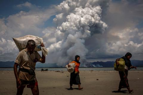 Smoke is seen on the Myanmar border as Rohingya refugees walk on the shore after crossing the Bangladesh-Myanmar border by boat through the Bay of Bengal, in Shah Porir Dwip, Bangladesh, September 11, 2017. PHOTO BY REUTERS/Danish Siddiqui