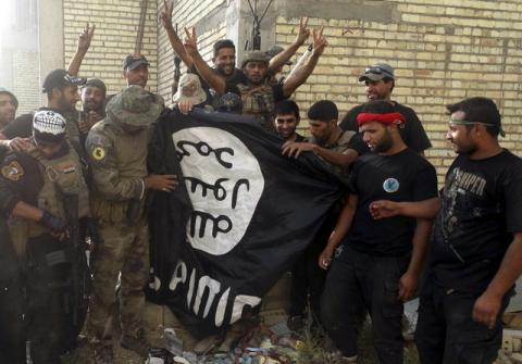 Iraqi security forces stand with an Islamist State flag which they pulled down at the University of Anbar, in Anbar province, July 26, 2015. PHOTO BY REUTERS/Stringer
