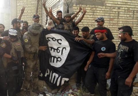 Iraqi security forces stand with an Islamist State flag which they pulled down at the University of Anbar, in Anbar province, July 26, 2015. PHOTO BY REUTERS/Stringer