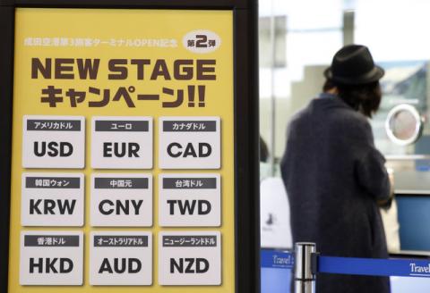Currency signs are seen at an exchange office as a woman exchanges money at Narita International airport, near Tokyo, Japan, March 25, 2016. PHOTO BY REUTERS/Yuya Shino