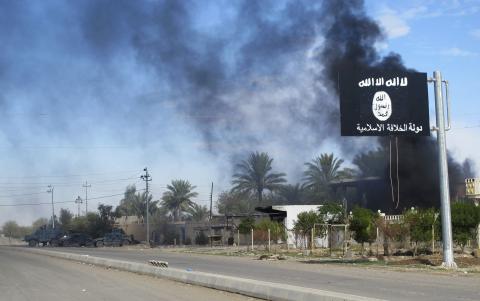 Smoke raises behind an Islamic State flag after Iraqi security forces and Shiite fighters took control of Saadiya in Diyala province from Islamist State militants, November 24, 2014. PHOTO BY REUTERS/Stringer