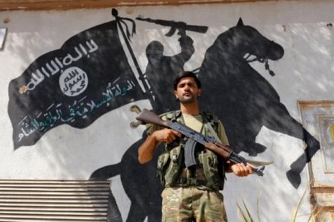 A member of Turkish-backed Free Syrian Army (FSA), seen with a mural of the Islamic State in the background, stands guard in front of a building in the border town of Jarablus, Syria, August 31, 2016. PHOTO BY REUTERS/Umit Bektas