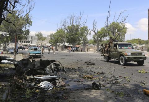 Somali government soldiers drive past the scene of a suicide car bomb attack next to a tea shop in the suburbs of capital Mogadishu