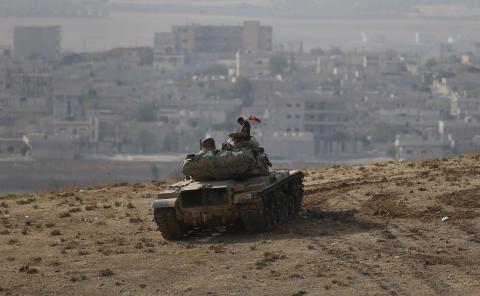 A Turkish soldier sits on top of a tank, with the Syrian town of Kobani in the background, as seen from the southeastern town of Suruc close to the Mursitpinar border crossing on the Turkish-Syrian border