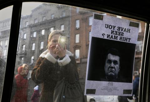 A woman takes photos of a "Wanted" notice for fugitive Ukrainian President Victor Yanukovich, plastered on the window of a car used as a barricade, near Kiev's Independent Square