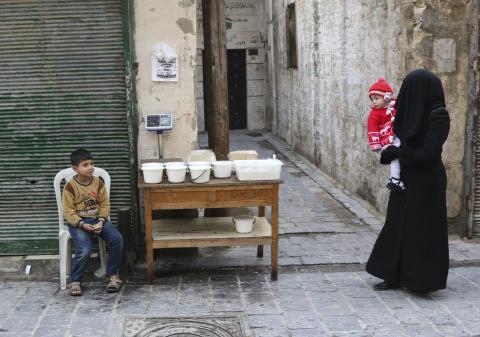 A woman carries a child as she walks past a boy selling yogurt along a street in Aleppo's Bab al-Hadeed district, December 10, 2014. PHOTO BY REUTERS/Mahmoud Hebbo