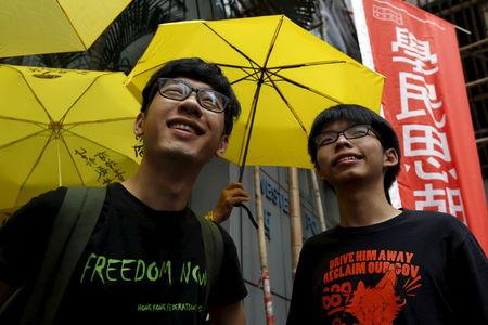 Student leaders Joshua Wong (R) and Nathan Law smile in front of supporters holding yellow umbrellas, symbol of the Occupy Central movement, outside a police station in Hong Kong, China, July 14, 2015. PHOTO BY REUTERS/Bobby Yip