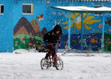 A stranded refugee boy rides his bicycle through a snowstorm at a refugee camp north of Athens, January 10, 2017. PHOTO BY REUTERS/Yannis Behrakis