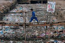 A boy walks past an electoral sign on a makeshift bridge, over a drainage channel littered with garbage, in a slum in Karachi, Pakistan, August 31, 2018. PHOTO BY REUTERS/Akhtar Soomro