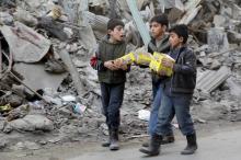 Boys carry boxes of biscuits near rubble of damaged buildings in Aleppo, Syria March 2, 2016. PHOTO BY REUTERS/Abdalrhman Ismail