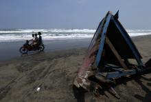 Children ride a motorcycle past a piece of wreckage of a boat which sank, at Agrabinta beach on the outskirts of Sukabumi
