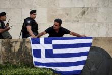 An anti-EU protester unfurls a Greek national flag next to riot police on the steps in front of the parliament building during a demonstration of about five hundred people in Athens, Greece, July 13, 2015. PHOTO BY REUTERS/Jean-Paul Pelissier