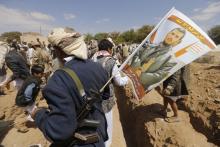 A follower of the Shi'ite Houthi group holds a flag, with the photo of the group's leader Abdul Malik al-Houthi on his rifle, during a mass funeral for victims of a suicide attack on followers of the Shi'ite Houthi group, in Sanaa
