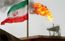 A gas flare on an oil production platform in the Soroush oil fields is seen alongside an Iranian flag in the Persian Gulf, Iran, July 25, 2005. PHOTO BY REUTERS/Raheb Homavandi