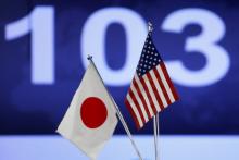 Japanese (L) and American flags are displayed in front of a monitor showing the Japanese yen's exchange rate against the U.S. dollar, in Tokyo, December 3, 2013. PHOTO BY REUTERS/Issei Kato