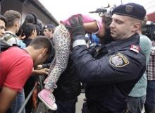 A police officer lifts up a young girl to prevent her from being crushed as migrants line-up to board trains at the railway station in Nickelsdorf, Austria September 5, 2015. PHOTO BY REUTERS/Srdjan Zivulovic