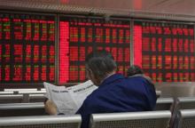 An investor reads the finance section of a newspaper in front of an electronic board showing stock information at a brokerage house in Beijing, China, September 21, 2015. PHOTO BY REUTERS/Stringer
