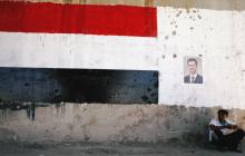 A man sits near a poster of Syrian President Bashar al-Assad during the re-opening of the road between Homs and Hama in Talbisi, Syria, June 6, 2018. PHOTO BY REUTERS/Omar Sanadiki