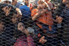 Migrants stand behind a gate as they wait to board buses inside a registration camp in Opatovac, Croatia, September 23, 2015. PHOTO BY REUTERS/Marko Djurica
