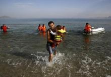 An Iranian migrant cries as while carrying his son after a small group of exhausted migrants from Iran arrived by paddling an engineless dinghy from the Turkish coast (seen in the background) at a beach on the Greek island of Kos, August 15, 2015. PHOTO BY REUTERS/Yannis Behrakis