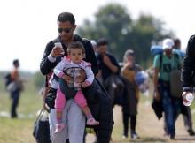A migrant uses his mobile phone carrying his child as he walks through fields with others next to a collection point near the Serbian Hungarian border in Roszke, Hungary, September 13, 2015. PHOTO BY REUTERS/Laszlo Balogh