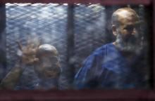 Muslim Brotherhood's senior member Mohamed El-Beltagy (L) gestures the four-fingered "Rabaa" hand symbol next to Islamist cleric Safwat Hegazis behind bars and glass panels from the defendant's cage, at a courtroom in Cairo