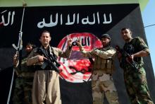 Kurdish Peshmerga fighters pose near a wall on which the black flag commonly used by Islamic State militants has been painted over, in the northern Iraqi town of Zumar, October 26, 2014, after having taken it from Islamic State. PHOTO BY REUTERS/Azad Lashkari