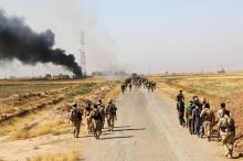 Kurdish Peshmerga fighters walk with their weapons as smoke rises from the site of clashes, south of Daquq, north of Baghdad, August 26, 2015. PHOTO BY REUTERS/Stringer