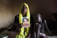 Rachel Daniel, 35, holds up a picture of her abducted daughter Rose Daniel, 17, as her son Bukar, 7, sits beside her at her home in Maiduguri