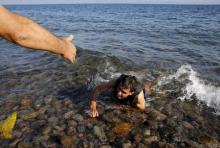 A local man helps a Syrian refugee who jumped off board from a dinghy as he swims exhausted at a beach on the Greek island of Lesbos, September 17, 2015. PHOTO BY REUTERS/Yannis Behrakis