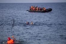 A man throws a rope to Syrian refugees swimming towards a beach after abandoning a dinghy with a broken engine on the Greek island of Lesbos, September 9, 2015. PHOTO BY REUTERS/Dimitris Michalakis