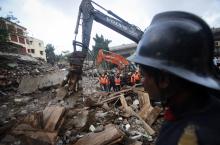 Rescue crew members watch as others use excavators to scour the debris for survivors at the site of a collapsed residential building in Mumbai