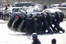 French riot police push an overturned car as striking French taxi drivers demonstrate at the Porte Maillot to block the traffic on the Paris ring road during a national protest against car-sharing service Uber, in Paris, June 25, 2015. PHOTO BY REUTERS/Charles Platiau