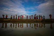 Rohingya refugees are reflected in rain water along an embankment next to paddy fields after fleeing from Myanmar into Palang Khali, near Cox's Bazar, Bangladesh, November 2, 2017. PHOTO BY REUTERS/Hannah McKay