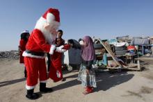 A volunteer wearing a Santa Claus costume distributes presents to children at a poor community in Najaf, south of Baghdad, December 19, 2015. PHOTO BY REUTERS/Alaa Al-Marjani