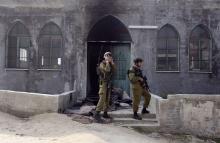 Israeli soldiers stand near the damaged door of a mosque, set ablaze by vandals, in the West Bank village of Urif, near Nablus