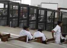 Suhayb Saad, an activist who rights groups say was taken by security forces and forced to confess on TV his membership of a terrorist cell, a reference to the Muslim Brotherhood, stands behind bars with other co-defendants as they wait to listen the ruling at a court in Cairo, June 23, 2014. PHOTO BY REUTERS/Asmaa Waguih