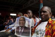 A supporter of former Ivory Coast President Laurent Gbagbo holds his portrait as he watches the trial on a screen with other supporters in Abidjan, January 28. 2016. PHOTO BY REUTERS/Luc Gnago