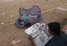 A supporter of Imran Khan, chairman of the Pakistan Tehreek-e-Insaf (PTI) political party, uses a hand fan as he sleeps in a mosquito tent while another reads newspaper in front of the Parliament building during what Khan dubbed as a "freedom march" in Islamabad